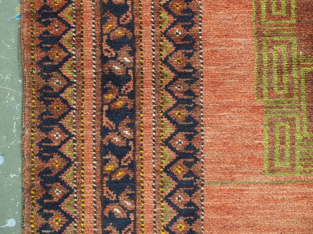 An antique hand-knotted Afghan Turkmen prayer rug featuring a central arch motif on a terracotta wool field framed by dark navy geometric borders. View V