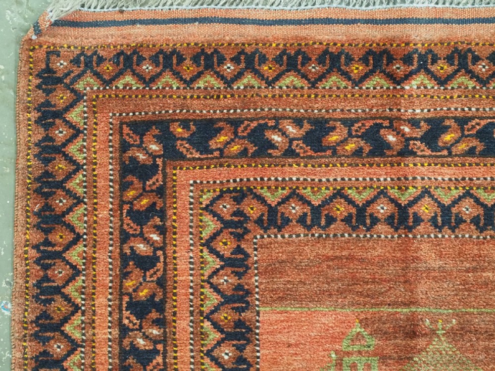 An antique hand-knotted Afghan Turkmen prayer rug featuring a central arch motif on a terracotta wool field framed by dark navy geometric borders. View VII