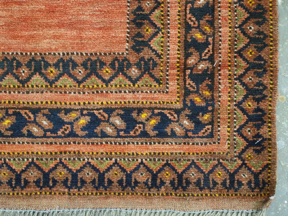 An antique hand-knotted Afghan Turkmen prayer rug featuring a central arch motif on a terracotta wool field framed by dark navy geometric borders. View X
