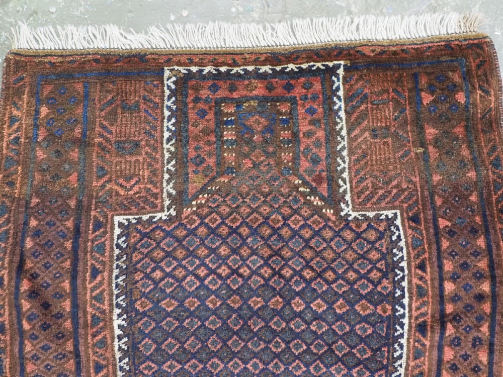 An antique hand-knotted wool Baluch prayer rug featuring a central mihrab niche surrounded by a diamond lattice pattern in dark red, navy blue, and brown tones with light fringe. View III