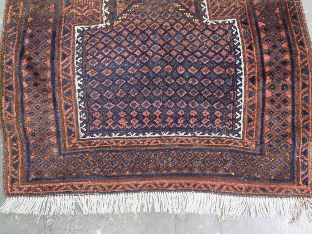 An antique hand-knotted wool Baluch prayer rug featuring a central mihrab niche surrounded by a diamond lattice pattern in dark red, navy blue, and brown tones with light fringe. View IV