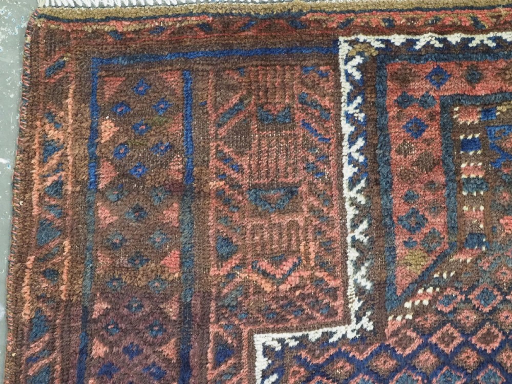 An antique hand-knotted wool Baluch prayer rug featuring a central mihrab niche surrounded by a diamond lattice pattern in dark red, navy blue, and brown tones with light fringe. View V