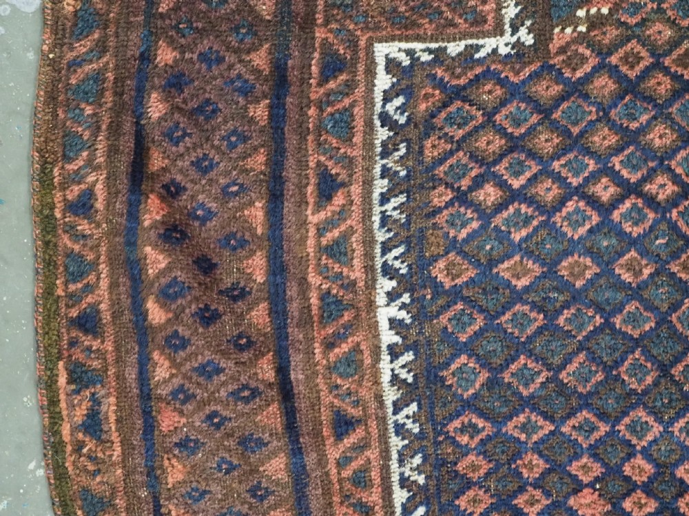 An antique hand-knotted wool Baluch prayer rug featuring a central mihrab niche surrounded by a diamond lattice pattern in dark red, navy blue, and brown tones with light fringe. View VI