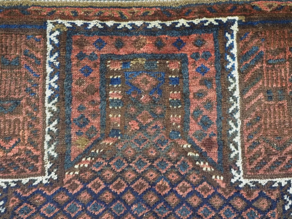 An antique hand-knotted wool Baluch prayer rug featuring a central mihrab niche surrounded by a diamond lattice pattern in dark red, navy blue, and brown tones with light fringe. View VII
