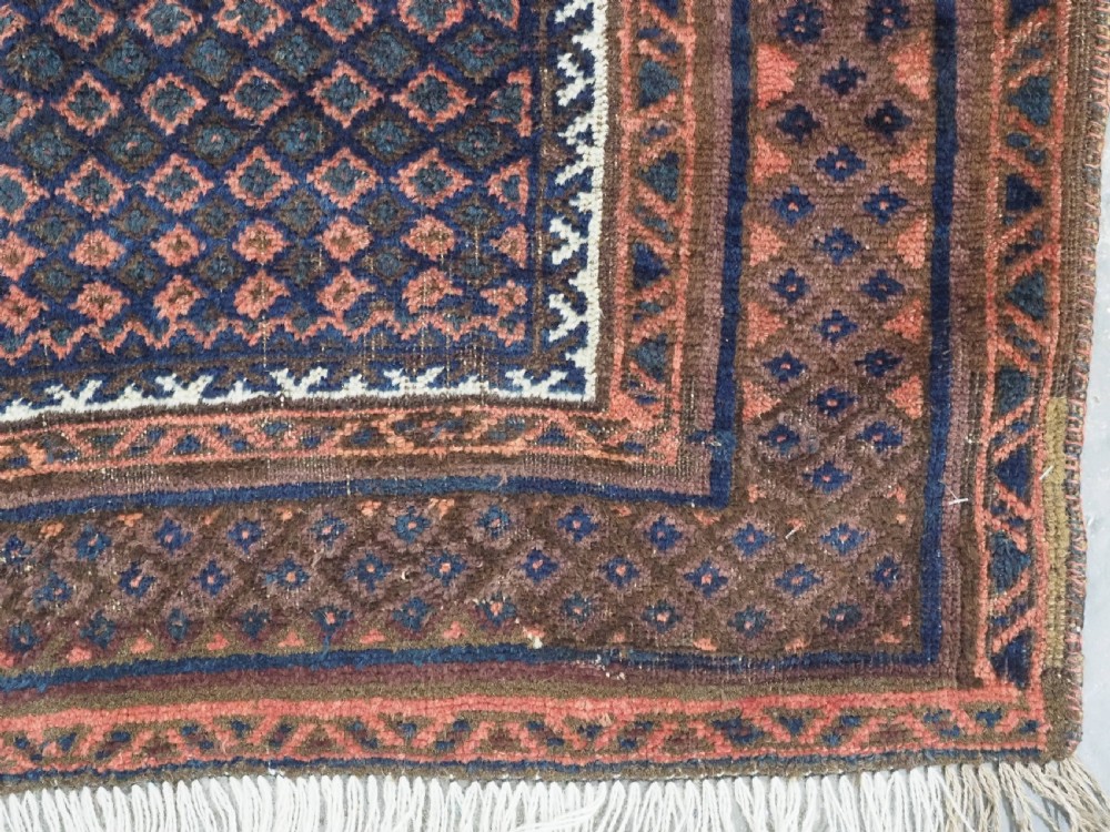 An antique hand-knotted wool Baluch prayer rug featuring a central mihrab niche surrounded by a diamond lattice pattern in dark red, navy blue, and brown tones with light fringe. View IX