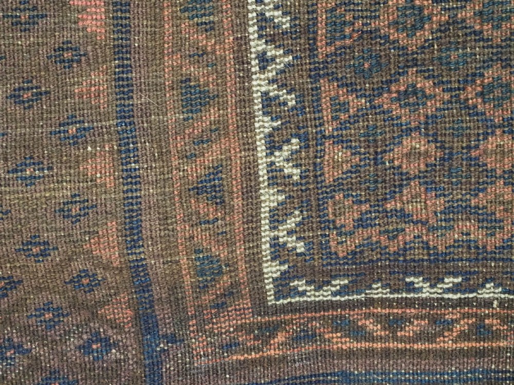 An antique hand-knotted wool Baluch prayer rug featuring a central mihrab niche surrounded by a diamond lattice pattern in dark red, navy blue, and brown tones with light fringe. View X