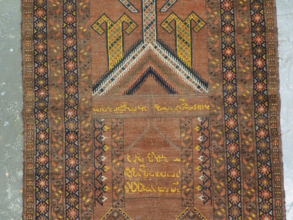 An antique hand-knotted Turkmen wool prayer rug featuring a terracotta-red field with geometric mihrab arches, woven script inscriptions, and patterned borders. View IV