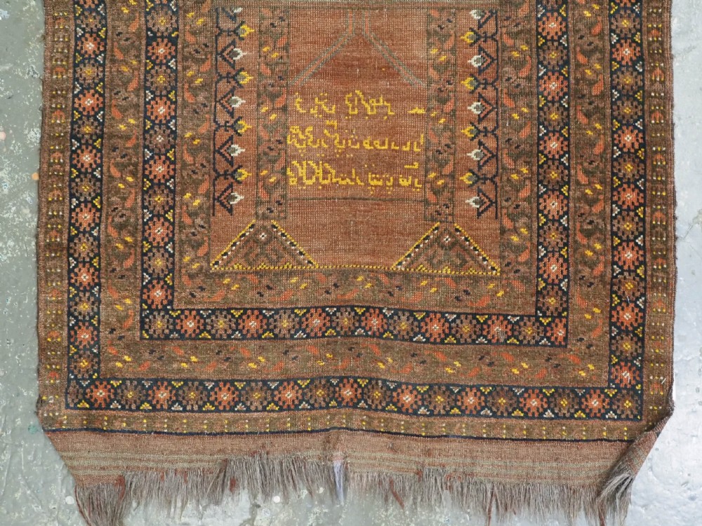 An antique hand-knotted Turkmen wool prayer rug featuring a terracotta-red field with geometric mihrab arches, woven script inscriptions, and patterned borders. View V