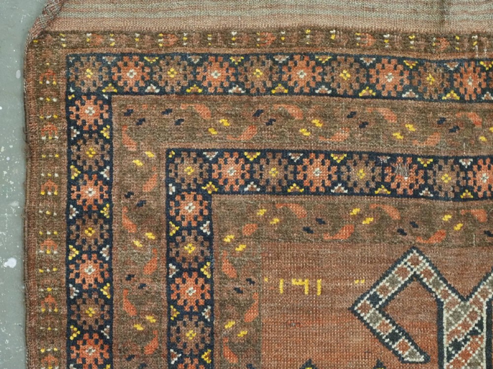 An antique hand-knotted Turkmen wool prayer rug featuring a terracotta-red field with geometric mihrab arches, woven script inscriptions, and patterned borders. View VI