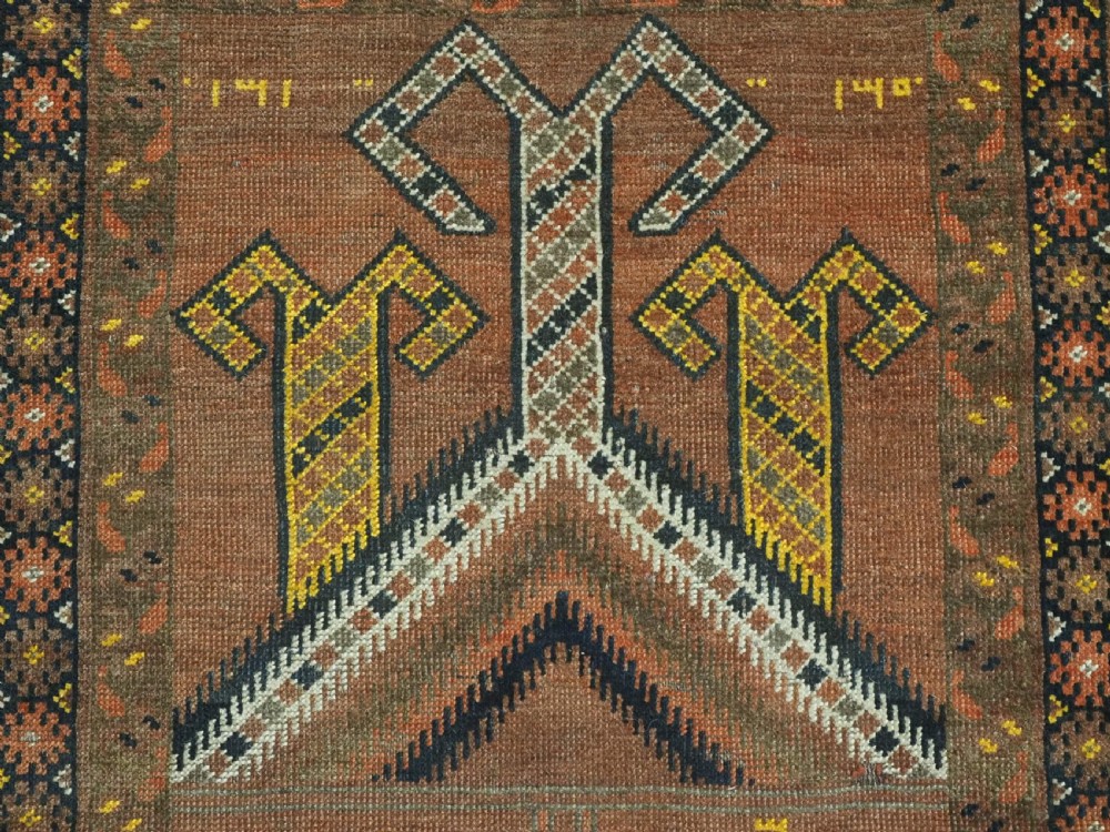 An antique hand-knotted Turkmen wool prayer rug featuring a terracotta-red field with geometric mihrab arches, woven script inscriptions, and patterned borders. View IX