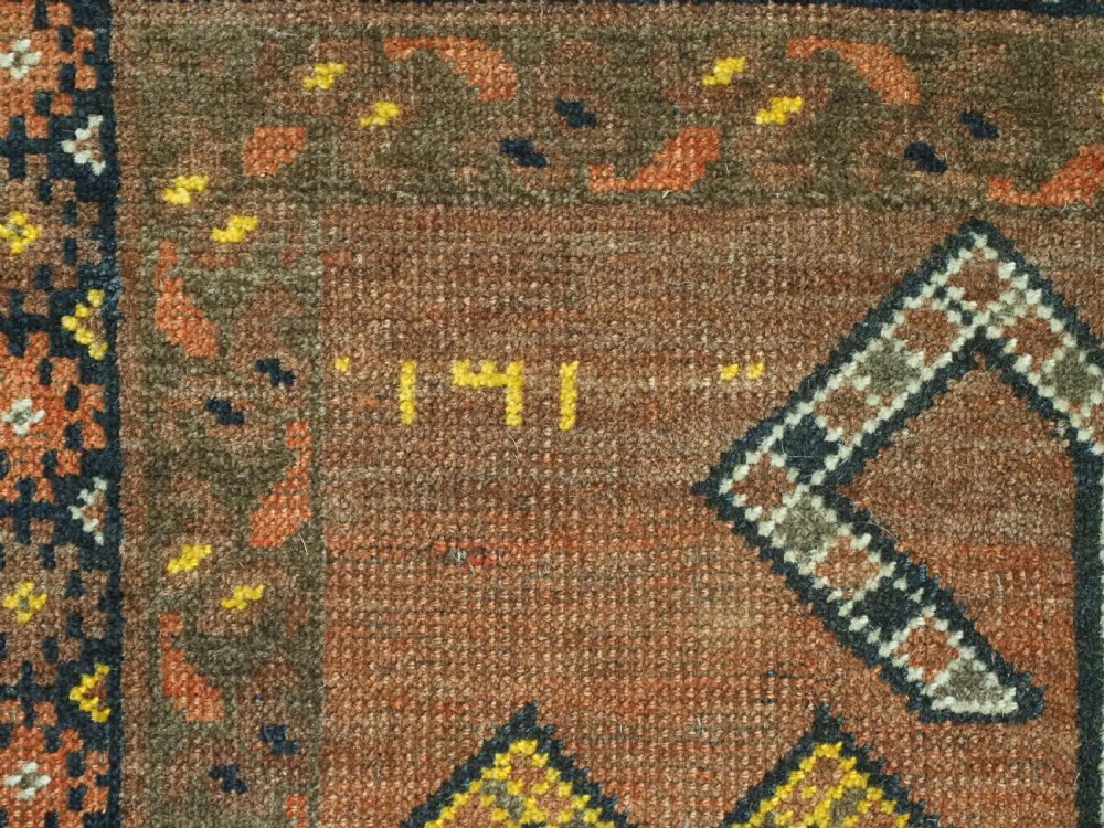 An antique hand-knotted Turkmen wool prayer rug featuring a terracotta-red field with geometric mihrab arches, woven script inscriptions, and patterned borders. View X