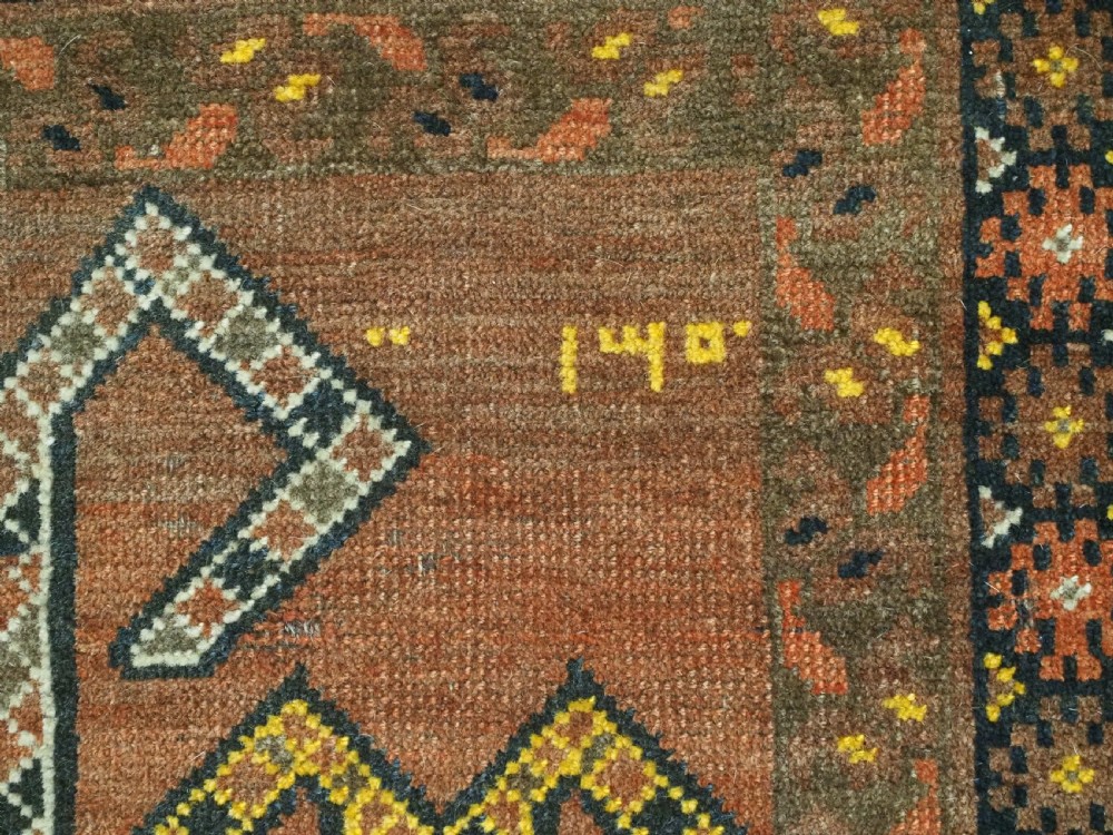 An antique hand-knotted Turkmen wool prayer rug featuring a terracotta-red field with geometric mihrab arches, woven script inscriptions, and patterned borders. View XI