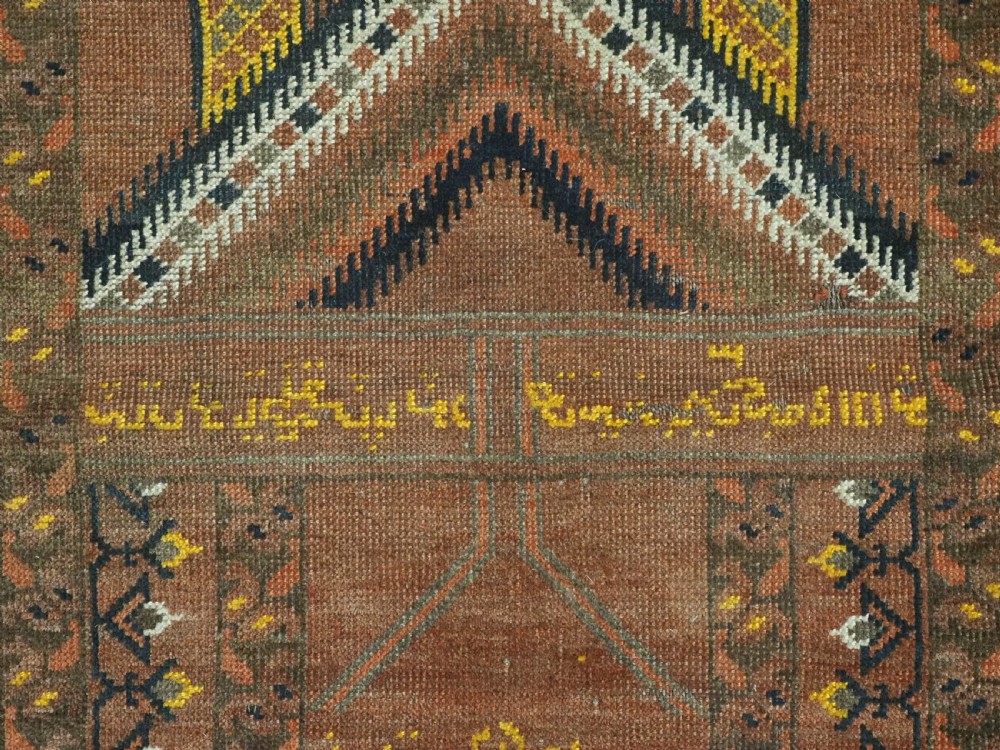 An antique hand-knotted Turkmen wool prayer rug featuring a terracotta-red field with geometric mihrab arches, woven script inscriptions, and patterned borders. View XII
