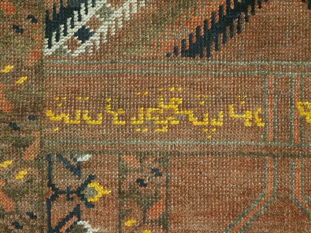 An antique hand-knotted Turkmen wool prayer rug featuring a terracotta-red field with geometric mihrab arches, woven script inscriptions, and patterned borders. View XIII