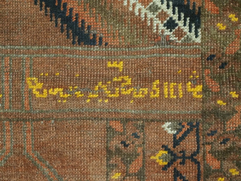 An antique hand-knotted Turkmen wool prayer rug featuring a terracotta-red field with geometric mihrab arches, woven script inscriptions, and patterned borders. View XIV
