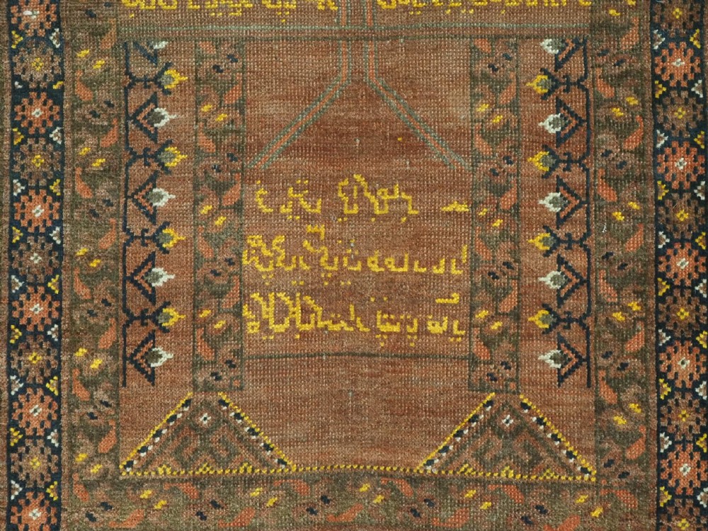 An antique hand-knotted Turkmen wool prayer rug featuring a terracotta-red field with geometric mihrab arches, woven script inscriptions, and patterned borders. View XV