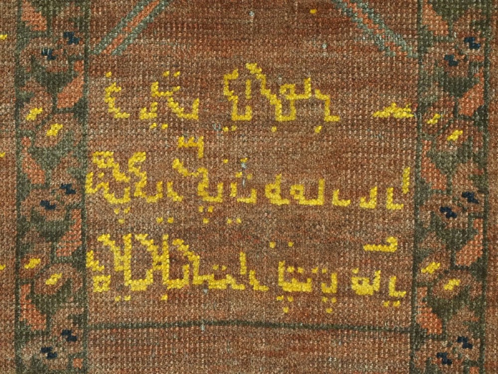 An antique hand-knotted Turkmen wool prayer rug featuring a terracotta-red field with geometric mihrab arches, woven script inscriptions, and patterned borders. View XVI