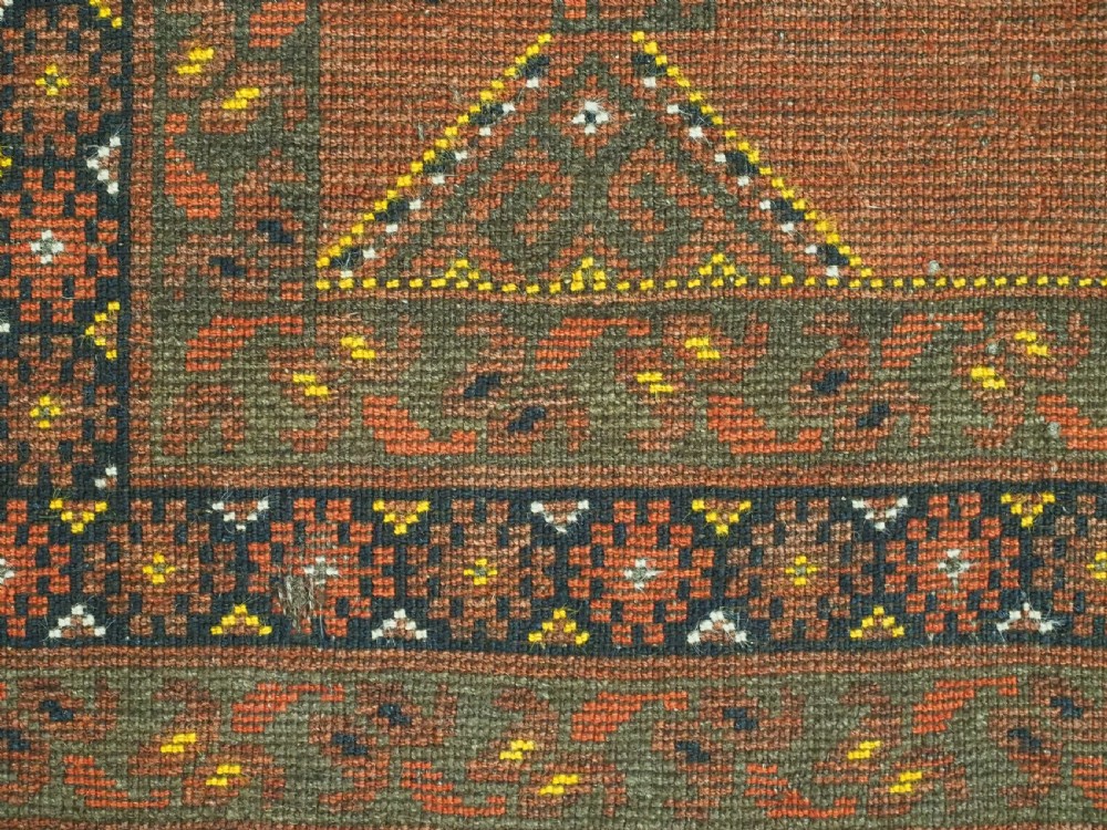An antique hand-knotted Turkmen wool prayer rug featuring a terracotta-red field with geometric mihrab arches, woven script inscriptions, and patterned borders. View XVIII