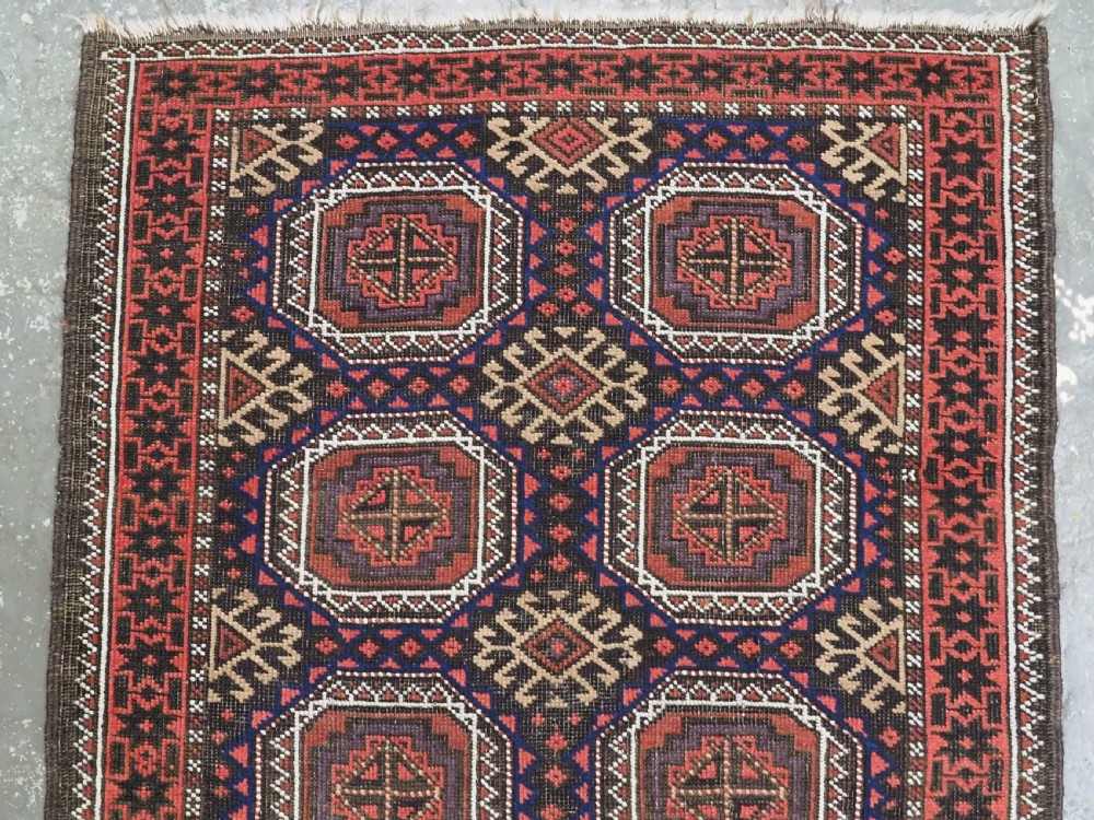 An antique Baluch hand-knotted wool rug with repeating octagonal geometric medallions in dark red, brown, and navy blue. View III