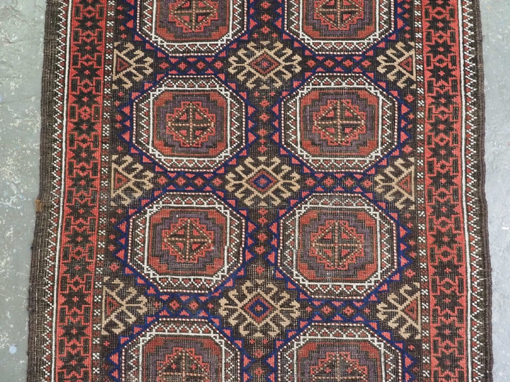 An antique Baluch hand-knotted wool rug with repeating octagonal geometric medallions in dark red, brown, and navy blue. View IV