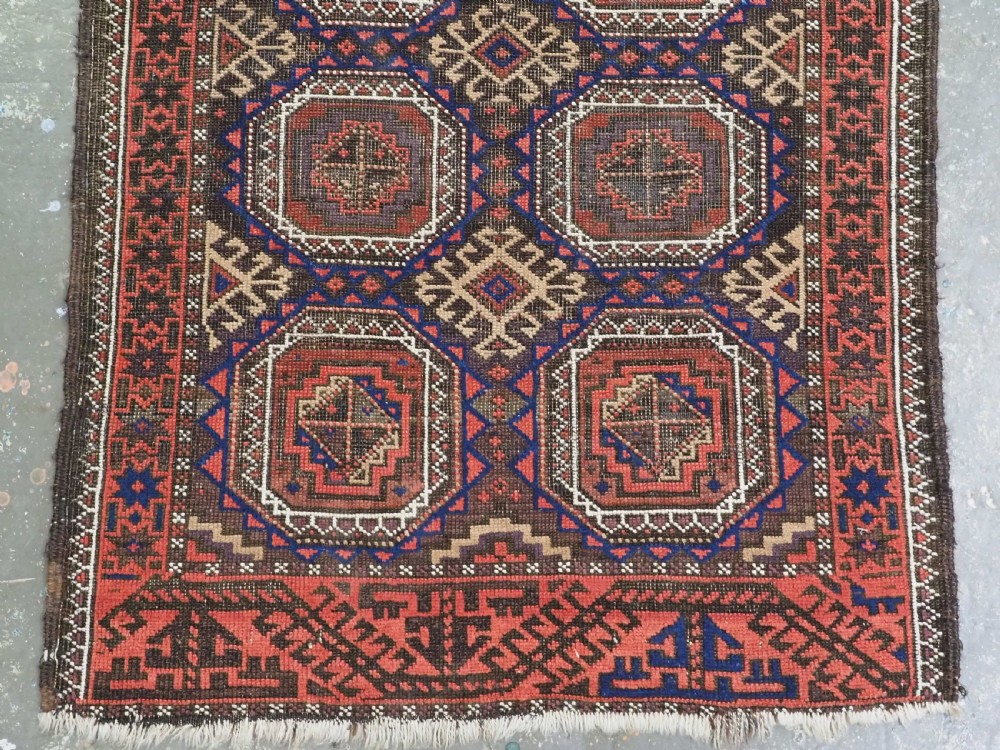 An antique Baluch hand-knotted wool rug with repeating octagonal geometric medallions in dark red, brown, and navy blue. View V
