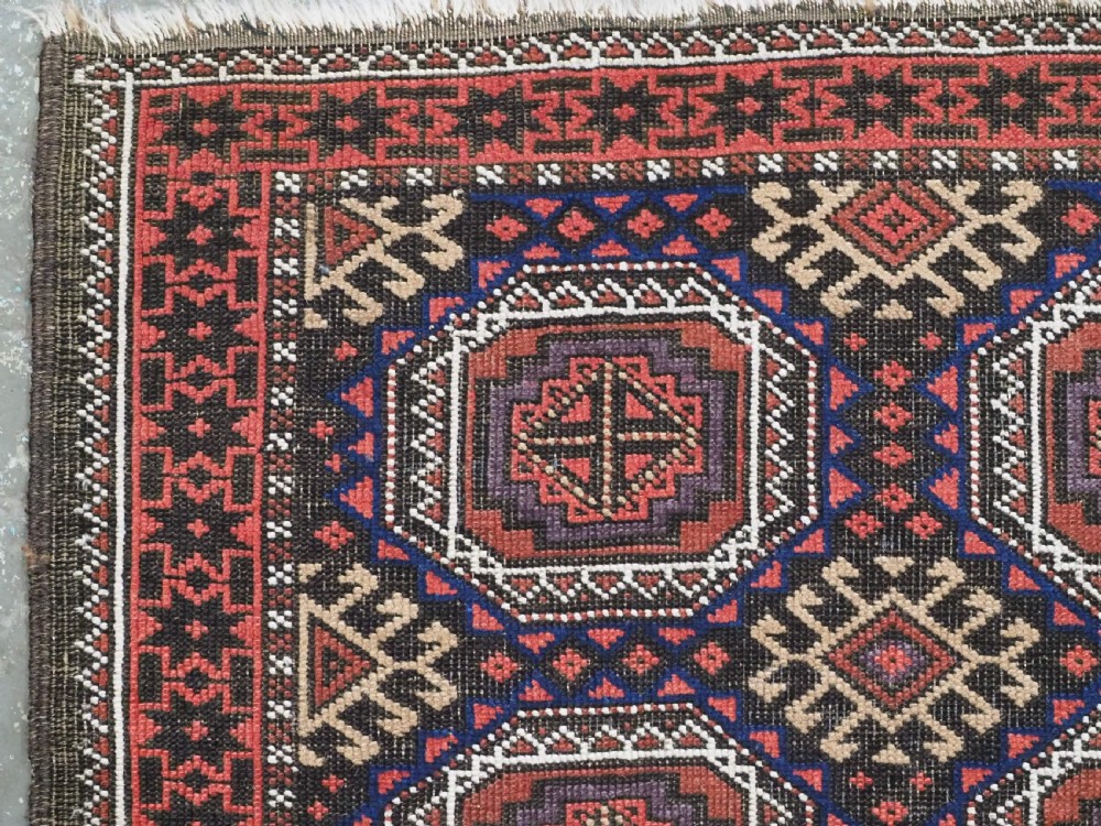 An antique Baluch hand-knotted wool rug with repeating octagonal geometric medallions in dark red, brown, and navy blue. View VI