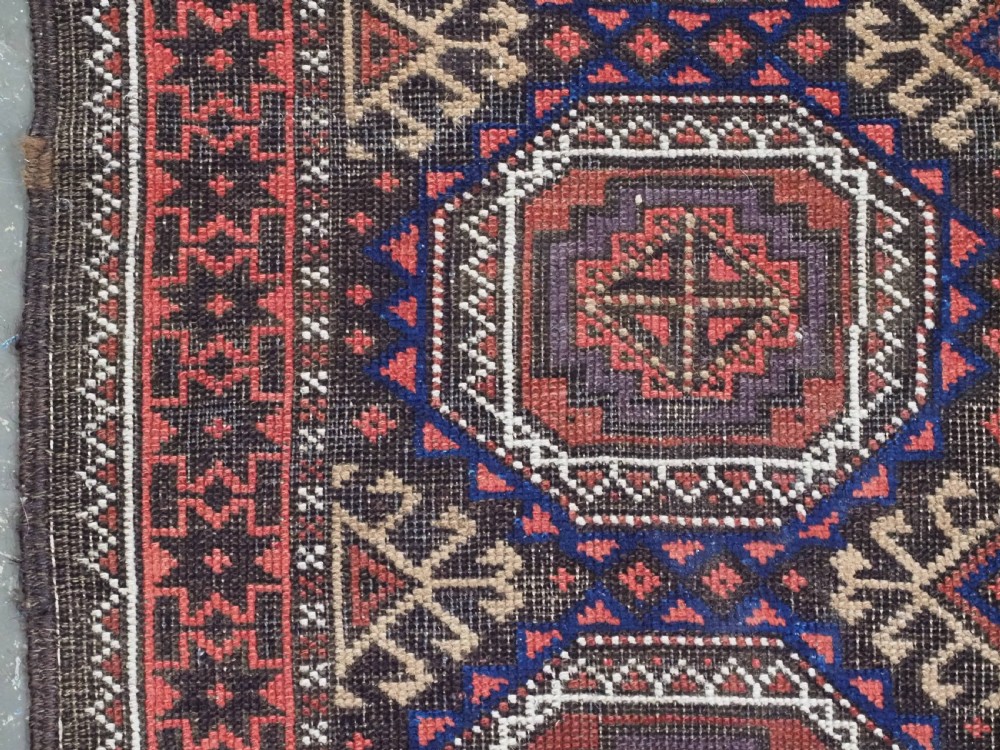 An antique Baluch hand-knotted wool rug with repeating octagonal geometric medallions in dark red, brown, and navy blue. View VII