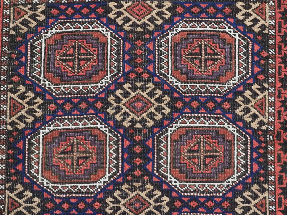 An antique Baluch hand-knotted wool rug with repeating octagonal geometric medallions in dark red, brown, and navy blue. View VIII
