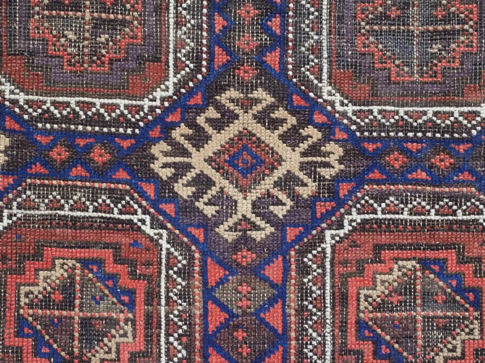 An antique Baluch hand-knotted wool rug with repeating octagonal geometric medallions in dark red, brown, and navy blue. View IX