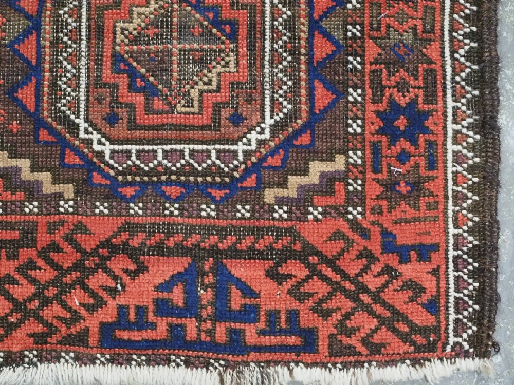 An antique Baluch hand-knotted wool rug with repeating octagonal geometric medallions in dark red, brown, and navy blue. View X