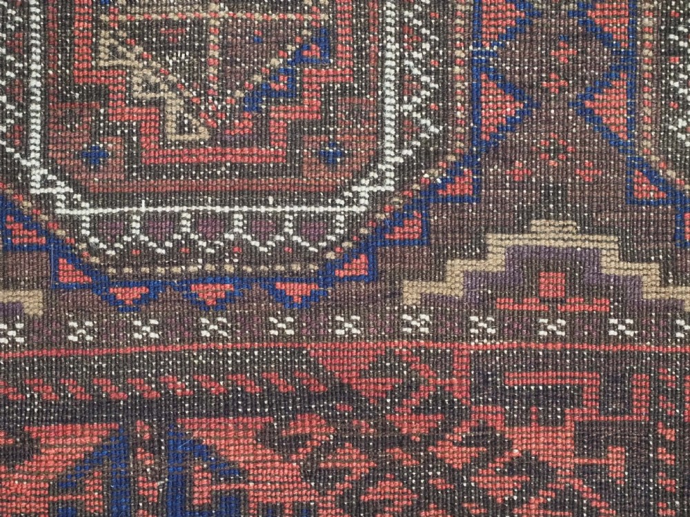An antique Baluch hand-knotted wool rug with repeating octagonal geometric medallions in dark red, brown, and navy blue. View XI