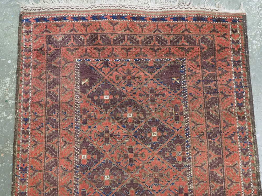 An antique hand-knotted Timuri Baluch rug featuring geometric diamond patterns in terracotta red, dark brown, and navy wool with fringed ends. View III