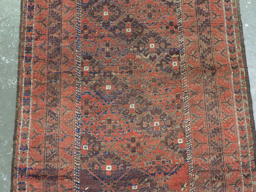 An antique hand-knotted Timuri Baluch rug featuring geometric diamond patterns in terracotta red, dark brown, and navy wool with fringed ends. View IV