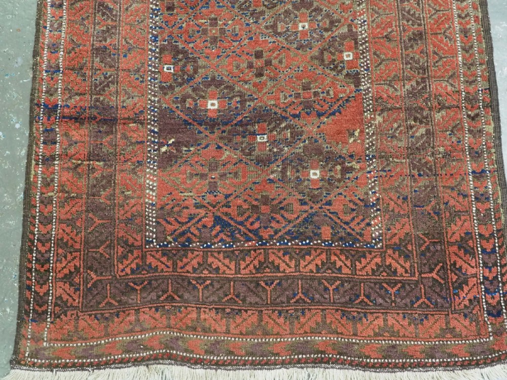An antique hand-knotted Timuri Baluch rug featuring geometric diamond patterns in terracotta red, dark brown, and navy wool with fringed ends. View V