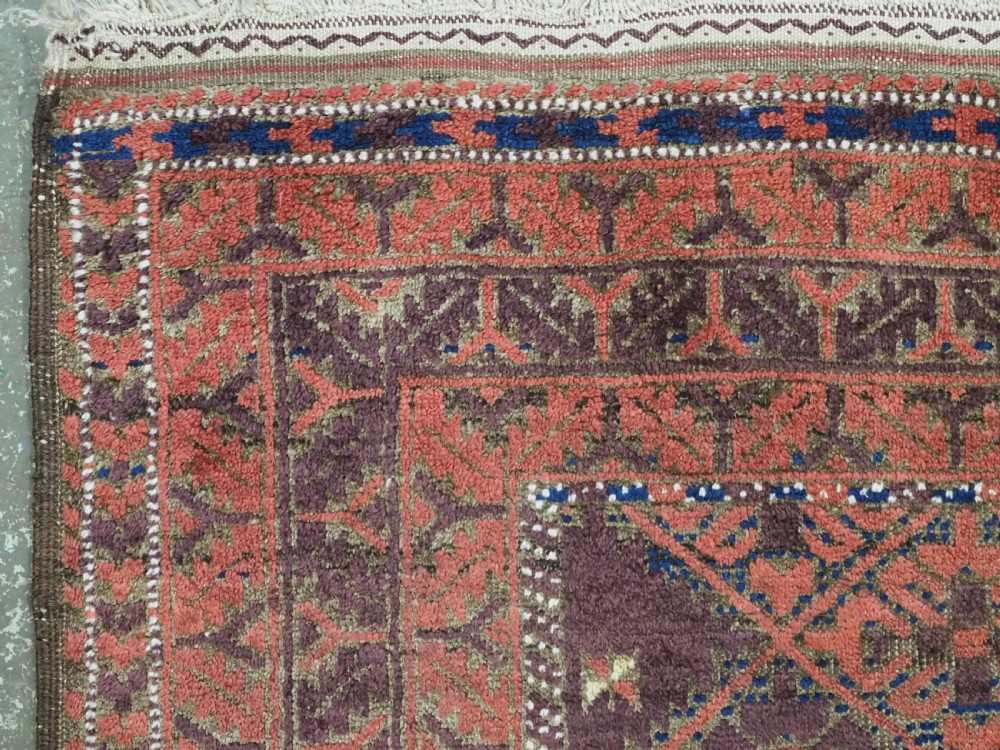 An antique hand-knotted Timuri Baluch rug featuring geometric diamond patterns in terracotta red, dark brown, and navy wool with fringed ends. View VI