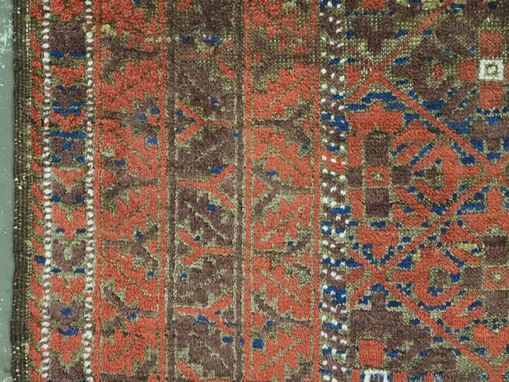 An antique hand-knotted Timuri Baluch rug featuring geometric diamond patterns in terracotta red, dark brown, and navy wool with fringed ends. View VII