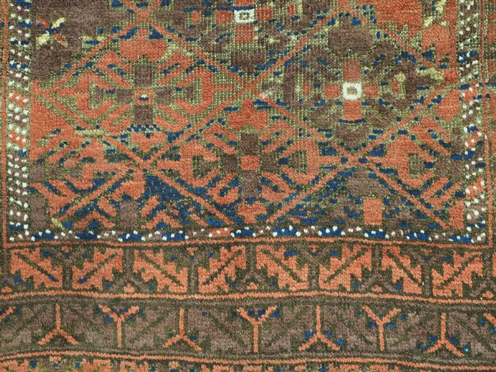 An antique hand-knotted Timuri Baluch rug featuring geometric diamond patterns in terracotta red, dark brown, and navy wool with fringed ends. View X