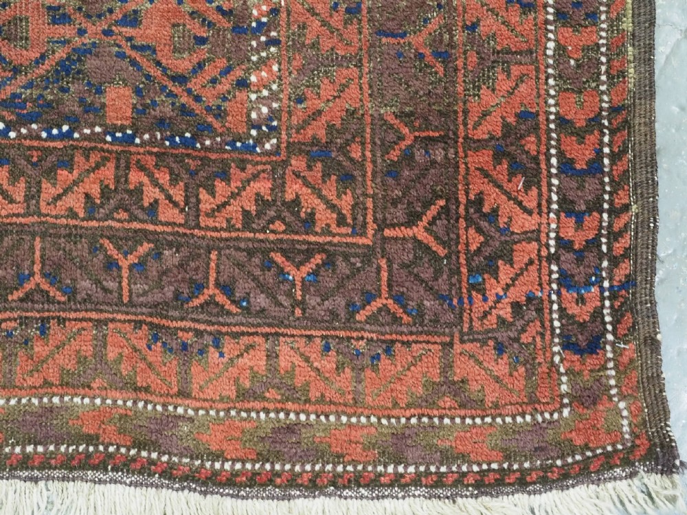 An antique hand-knotted Timuri Baluch rug featuring geometric diamond patterns in terracotta red, dark brown, and navy wool with fringed ends. View XI
