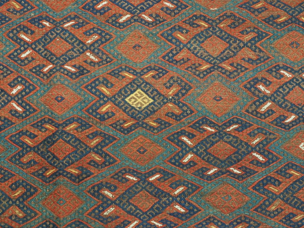 A rectangular handwoven wool kilim rug featuring a dense geometric diamond lattice pattern in terracotta red, navy blue, and cream with wide plain-woven border ends. View IX