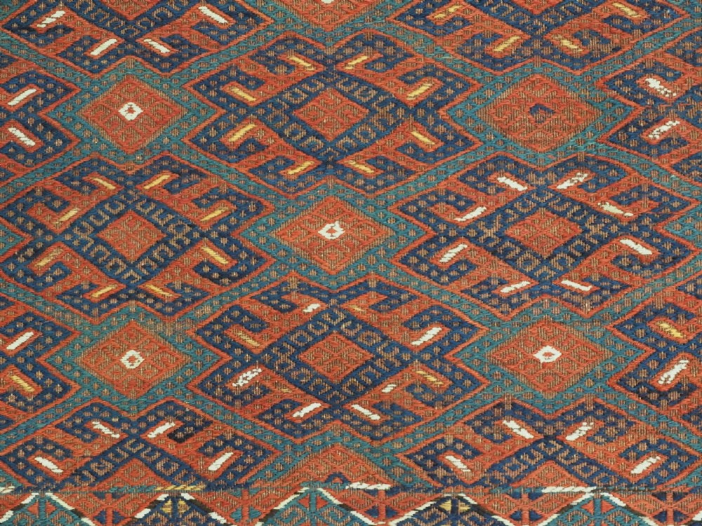 A rectangular handwoven wool kilim rug featuring a dense geometric diamond lattice pattern in terracotta red, navy blue, and cream with wide plain-woven border ends. View XI