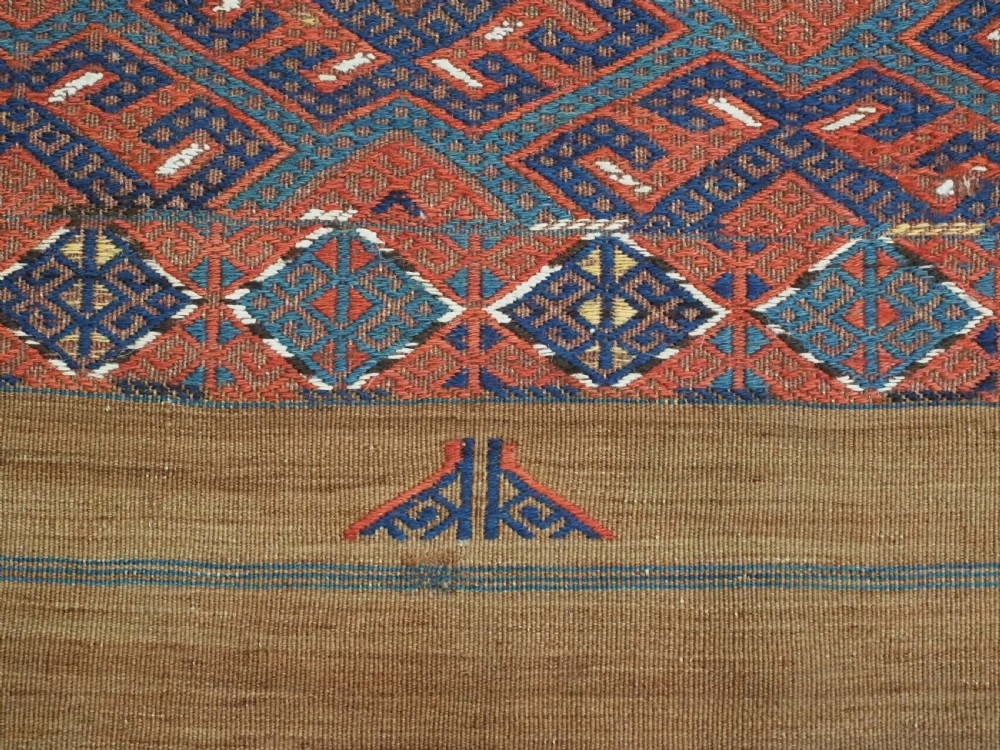 A rectangular handwoven wool kilim rug featuring a dense geometric diamond lattice pattern in terracotta red, navy blue, and cream with wide plain-woven border ends. View XII