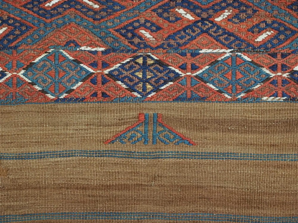 A rectangular handwoven wool kilim rug featuring a dense geometric diamond lattice pattern in terracotta red, navy blue, and cream with wide plain-woven border ends. View XIII