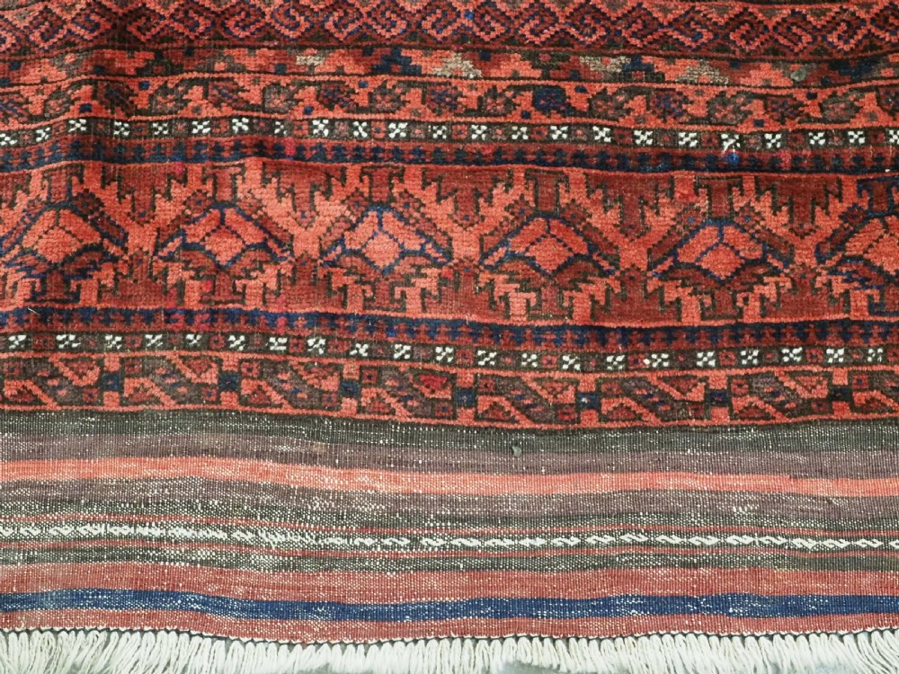An antique hand-knotted Baluch wool main carpet featuring a deep red field with repeated dark blue geometric motifs and multi-bordered edges. View VIII