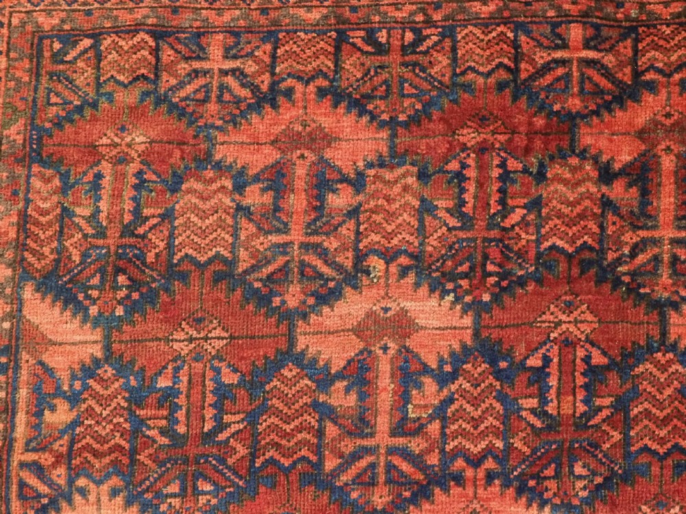 An antique hand-knotted Baluch wool main carpet featuring a deep red field with repeated dark blue geometric motifs and multi-bordered edges. View XI
