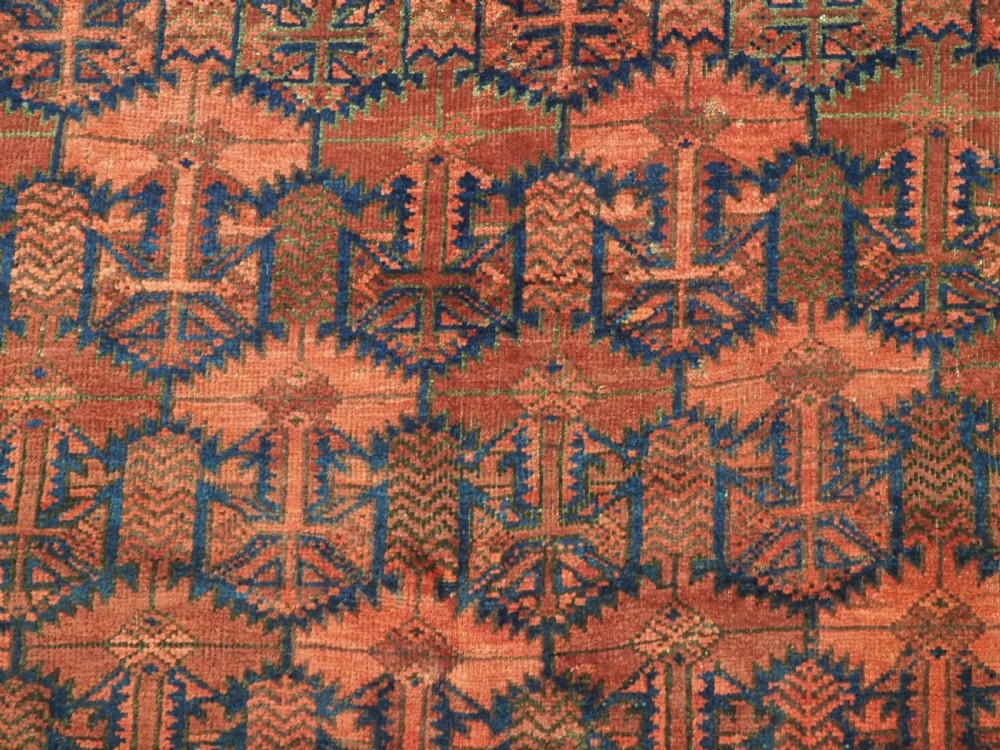 An antique hand-knotted Baluch wool main carpet featuring a deep red field with repeated dark blue geometric motifs and multi-bordered edges. View XII