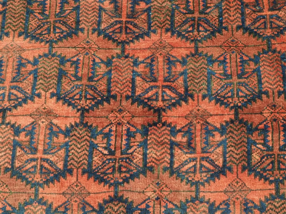 An antique hand-knotted Baluch wool main carpet featuring a deep red field with repeated dark blue geometric motifs and multi-bordered edges. View XIII