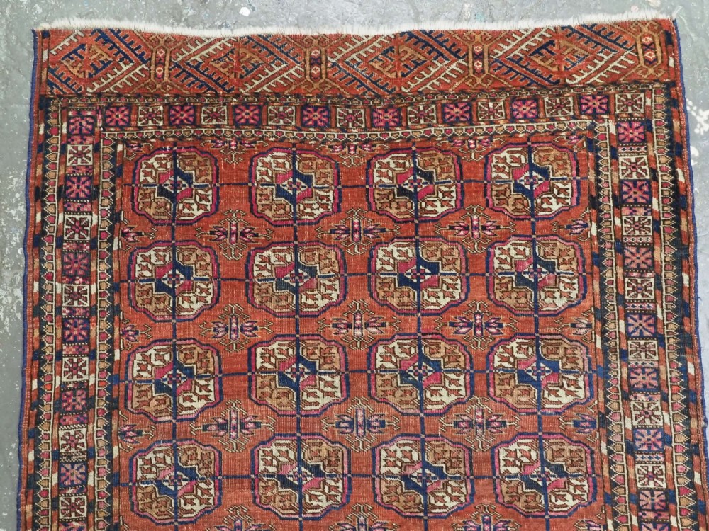 An antique Tekke Turkmen hand-knotted wool rug featuring repeating octagonal gul motifs on a deep brick red background with geometric borders. View III