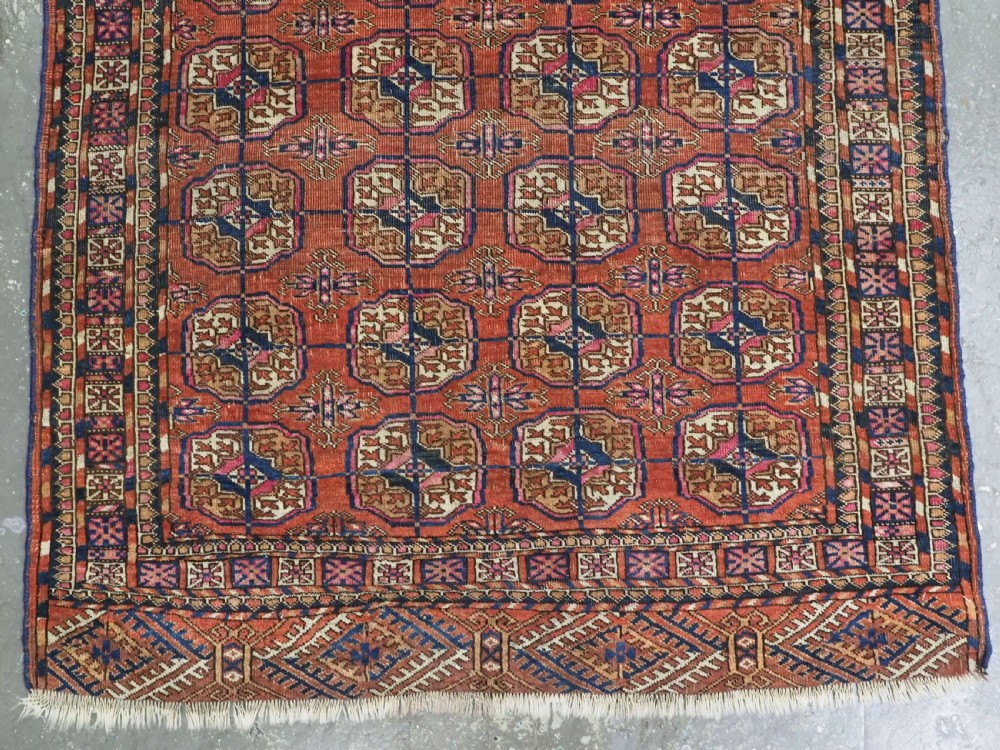 An antique Tekke Turkmen hand-knotted wool rug featuring repeating octagonal gul motifs on a deep brick red background with geometric borders. View IV
