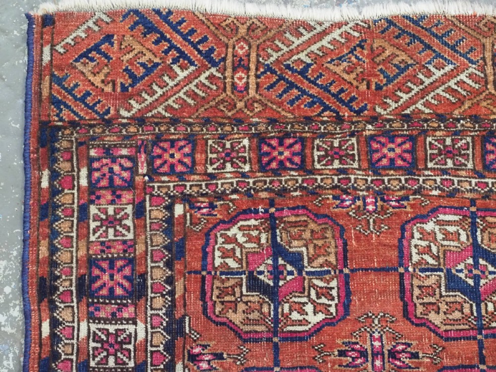 An antique Tekke Turkmen hand-knotted wool rug featuring repeating octagonal gul motifs on a deep brick red background with geometric borders. View V