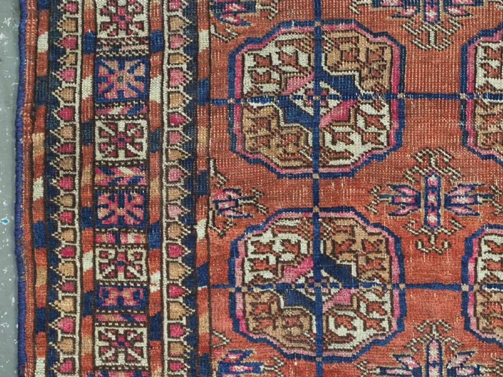 An antique Tekke Turkmen hand-knotted wool rug featuring repeating octagonal gul motifs on a deep brick red background with geometric borders. View VI
